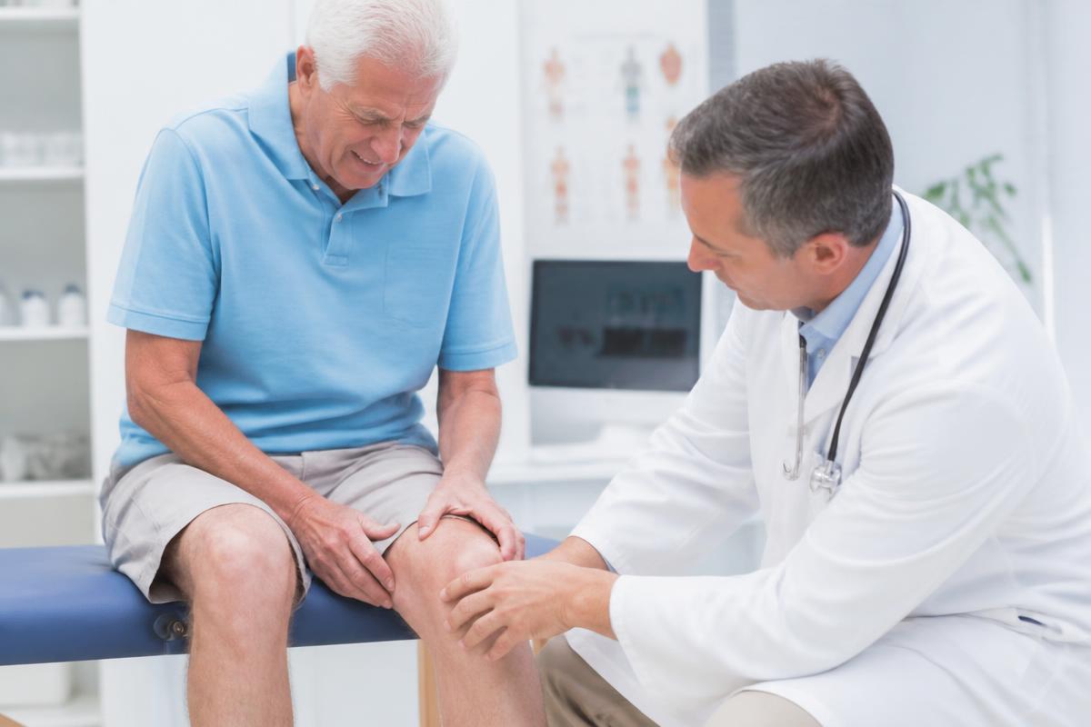 Paciente mayor sujetándose la rodilla mientras el médico examina la articulación